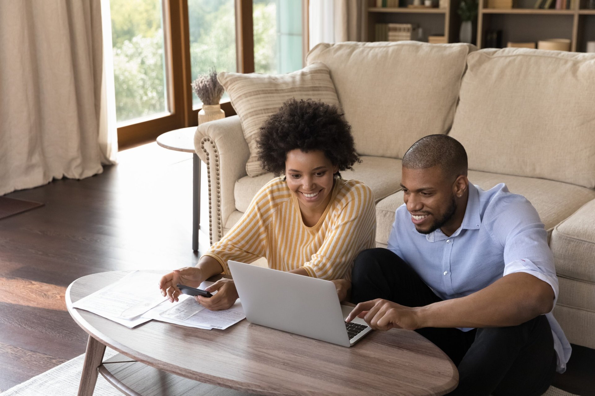 Excited happy couple looking at laptop while sitting on the floor at home