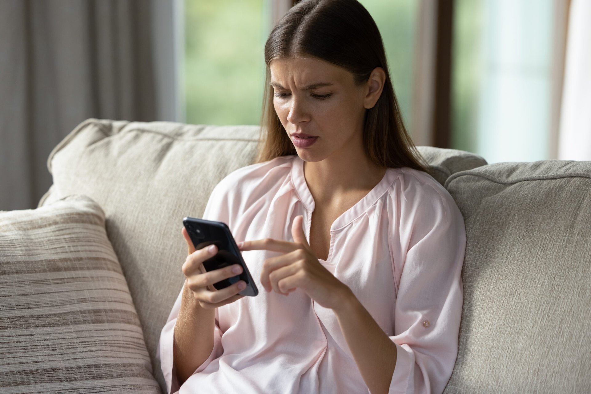 Woman on couch looking at her cell phone confused.
