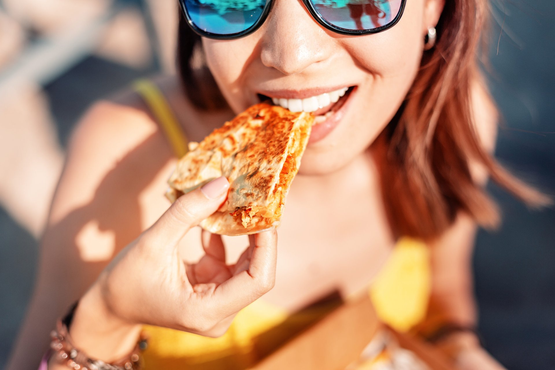 Girl in sunglasses eating a quesadilla.