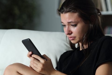 Crying woman who is sad using her smartphone or cell phone and upset texting
