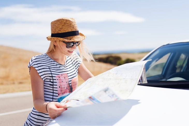 Young woman studying map by car on highway.