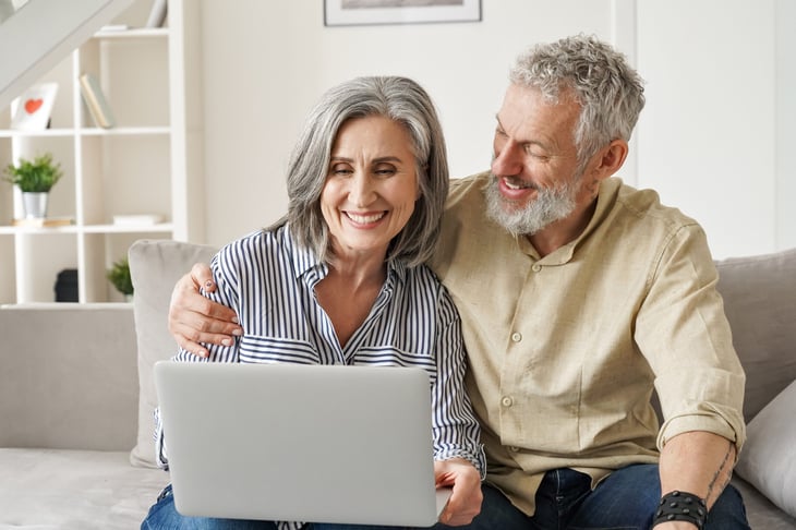 Happy older couple looking at and talking about their finances on laptop.