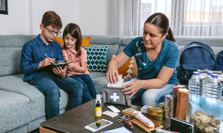 Mother preparing emergency backpack with her children in the living room